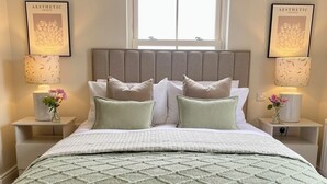 Un dormitorio con una cama, dos mesitas de noche, un ventanal y cuadros en las paredes.