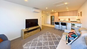 A modern living room with a flat-screen TV, a sofa, and a kitchen area with bar stools. - Chic and Comfy 1 Bedroom in Manchester Street (Christchurch)