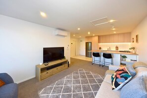 A modern living room with a flat-screen TV, a sofa, and a kitchen area with bar stools. - Chic and Comfy 1 Bedroom in Manchester Street (Christchurch)