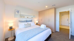 A hotel room with a bed, bedside lamps, a shelf with decorative items, and a wardrobe. - Chic and Comfy 1 Bedroom in Manchester Street (Christchurch)