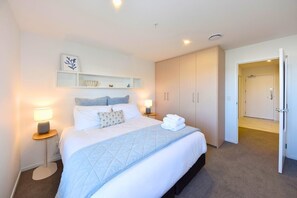 A hotel room with a bed, bedside lamps, a shelf with decorative items, and a wardrobe. - Chic and Comfy 1 Bedroom in Manchester Street (Christchurch)
