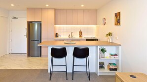 A modern kitchen with a central island, two bar stools, a refrigerator, and a bookshelf. - Chic and Comfy 1 Bedroom in Manchester Street (Christchurch)