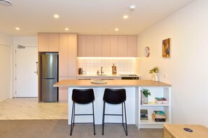 A modern kitchen with a central island, two bar stools, a refrigerator, and a bookshelf. - Chic and Comfy 1 Bedroom in Manchester Street (Christchurch)