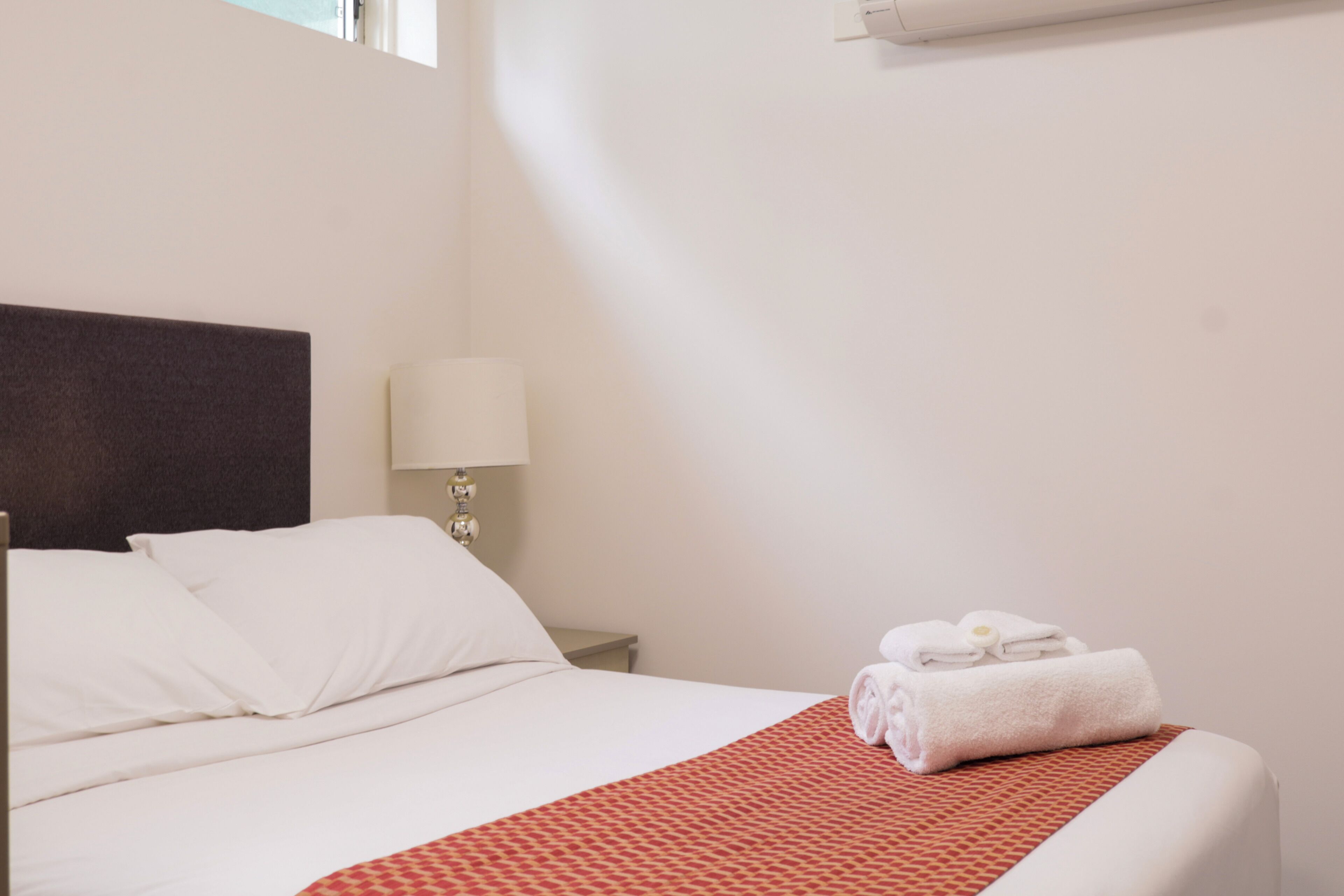 A hotel room with a bed, a nightstand, a lamp, and a window.