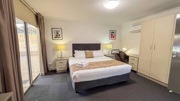 A hotel room with a bed, two bedside tables with lamps, a desk, a chair, a wardrobe, and a large window with curtains.