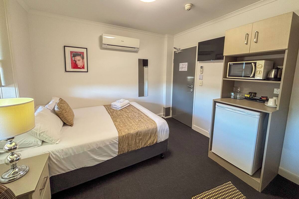 Une chambre d’hôtel équipée d’un lit, d’une table de chevet, d’une lampe, d’un climatiseur, d’un four à micro-ondes et d’un petit réfrigérateur.