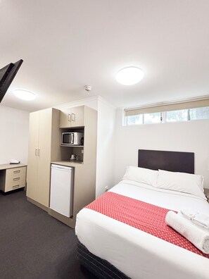 A hotel room with a bed, a kitchenette, a desk, and a window. - Hotel Gracelands (Parkes)