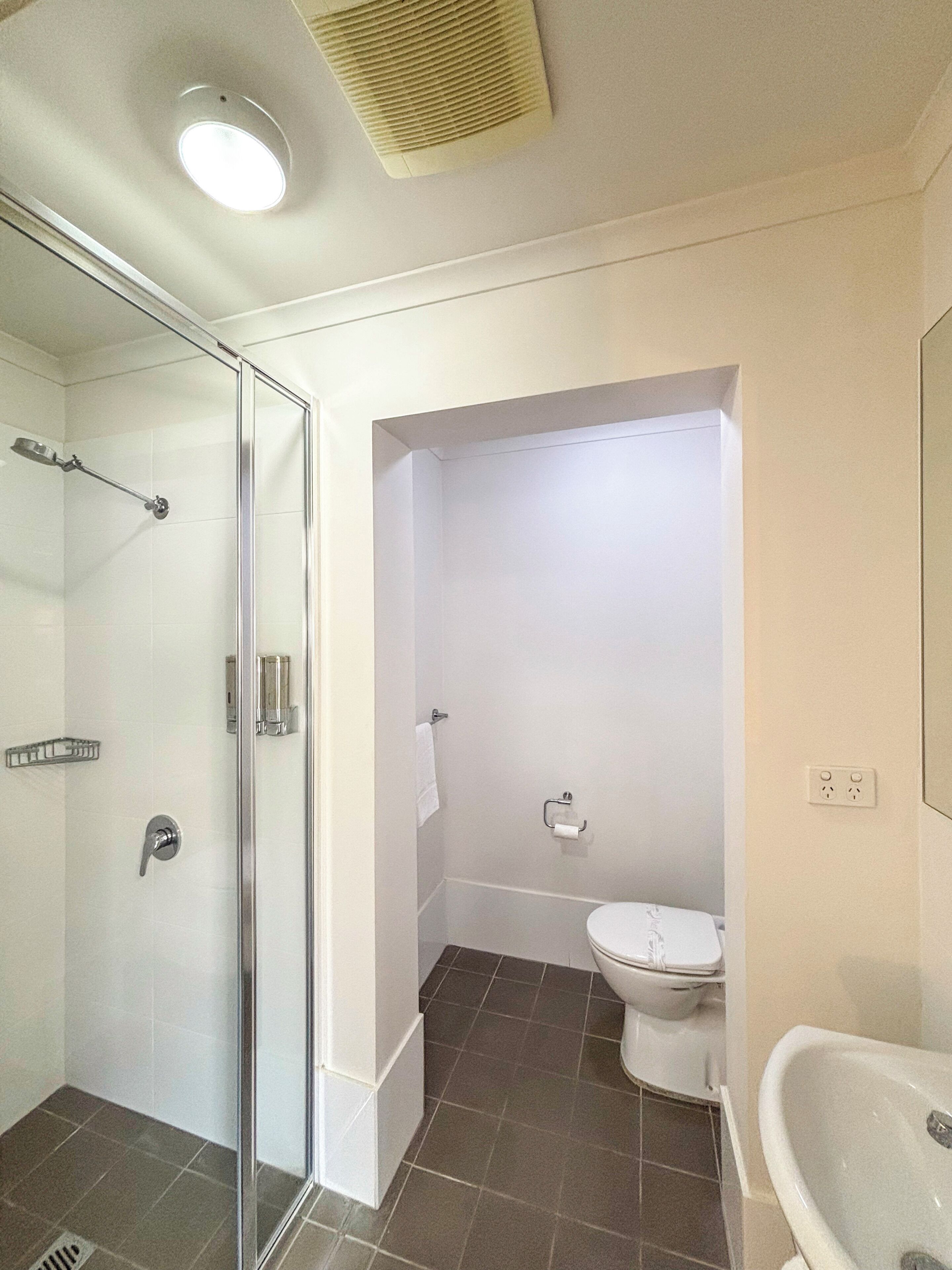 Een badkamer met een douchecabine van glas, een toilet en een wastafel.