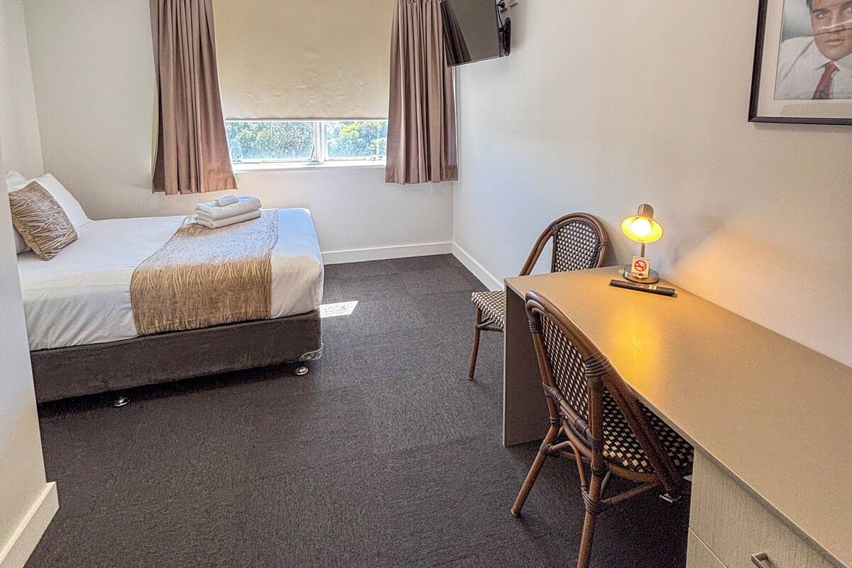 Une chambre d’hôtel équipée d’un lit, d’un bureau, d’une chaise, d’une télévision et d’une fenêtre avec des rideaux.