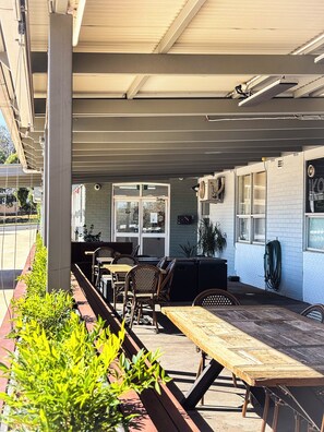 An outdoor seating area with tables and chairs, a covered roof, and a brick wall. - Hotel Gracelands (Parkes)