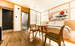 A hotel room with a bed, a small table, two chairs, a wooden floor, a sliding door, and a painting on the wall. - Daeheung Manwol Hotel (Daejeon)