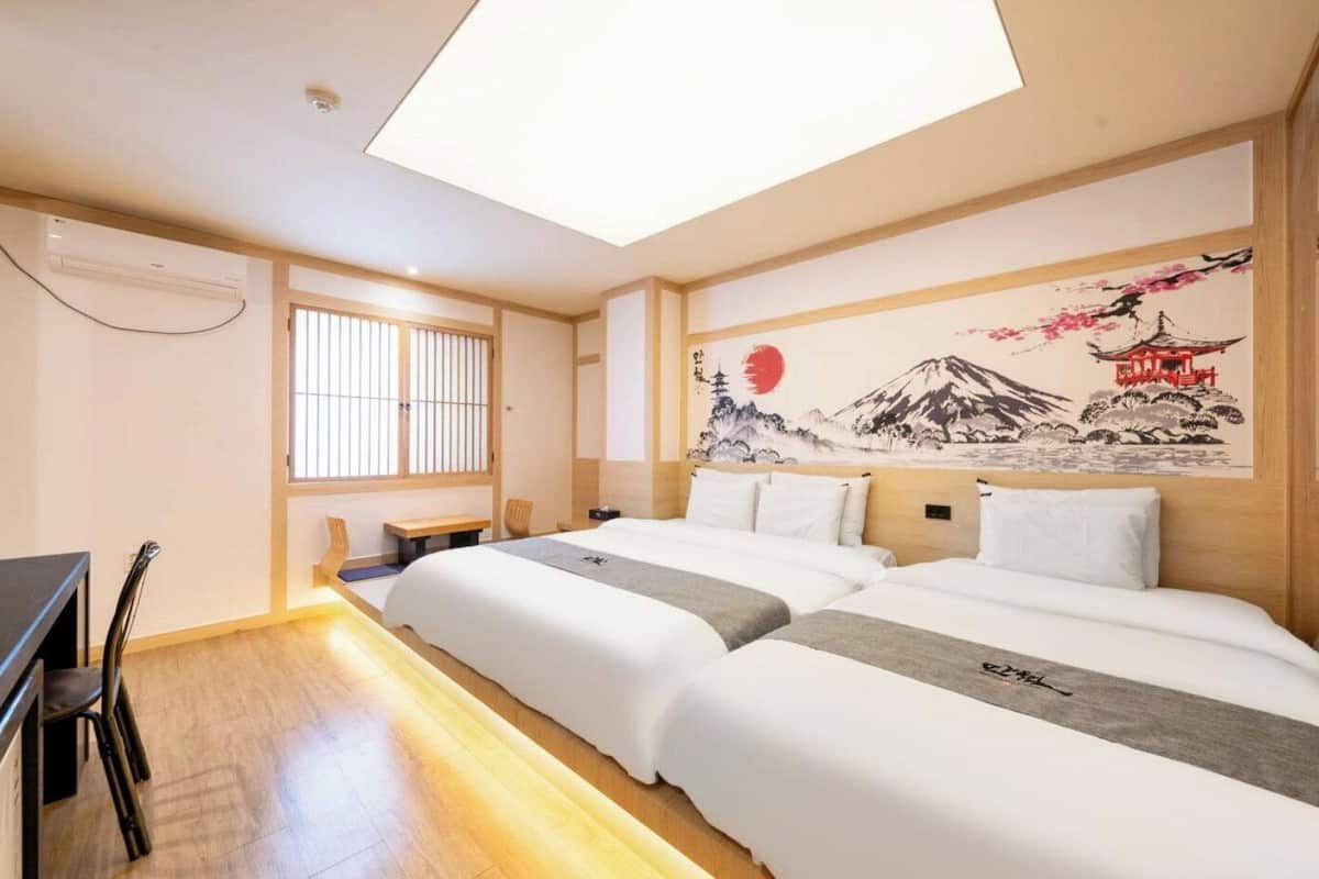 A hotel room with a large bed, a desk, and a window with blinds.