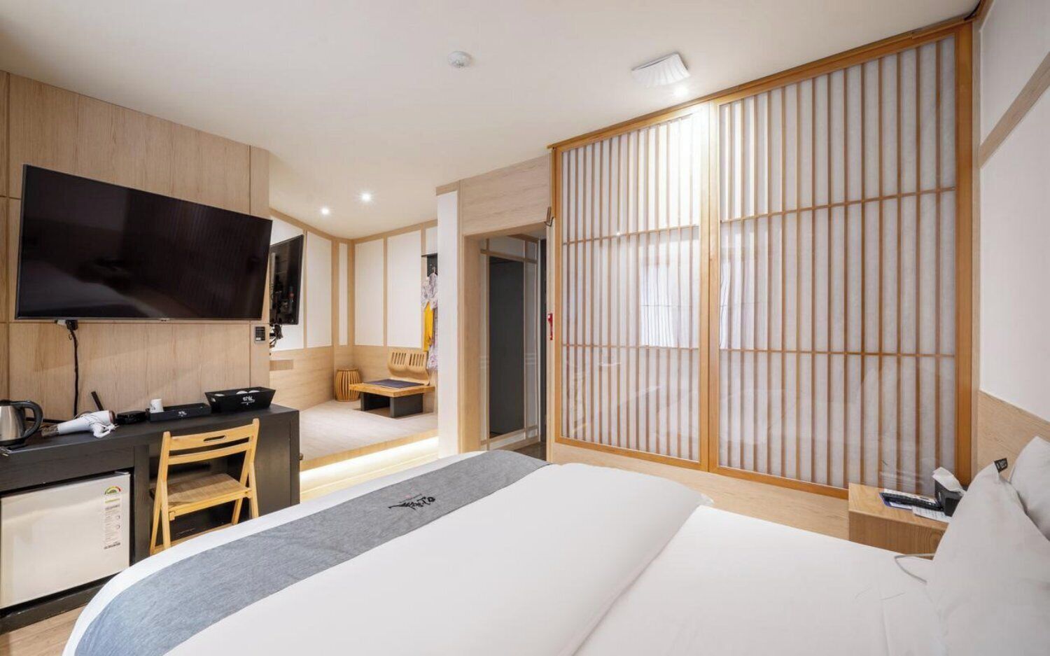 A modern hotel room with a bed, desk, chair, television, and sliding shoji screen.