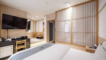 A modern hotel room with a bed, desk, chair, television, and sliding shoji screen.