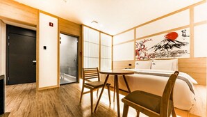 A hotel room with a wooden floor, a bed with white bedding, a small round table, two chairs, a sliding door, and a wall with a painting. - Daeheung Manwol Hotel (Daejeon)