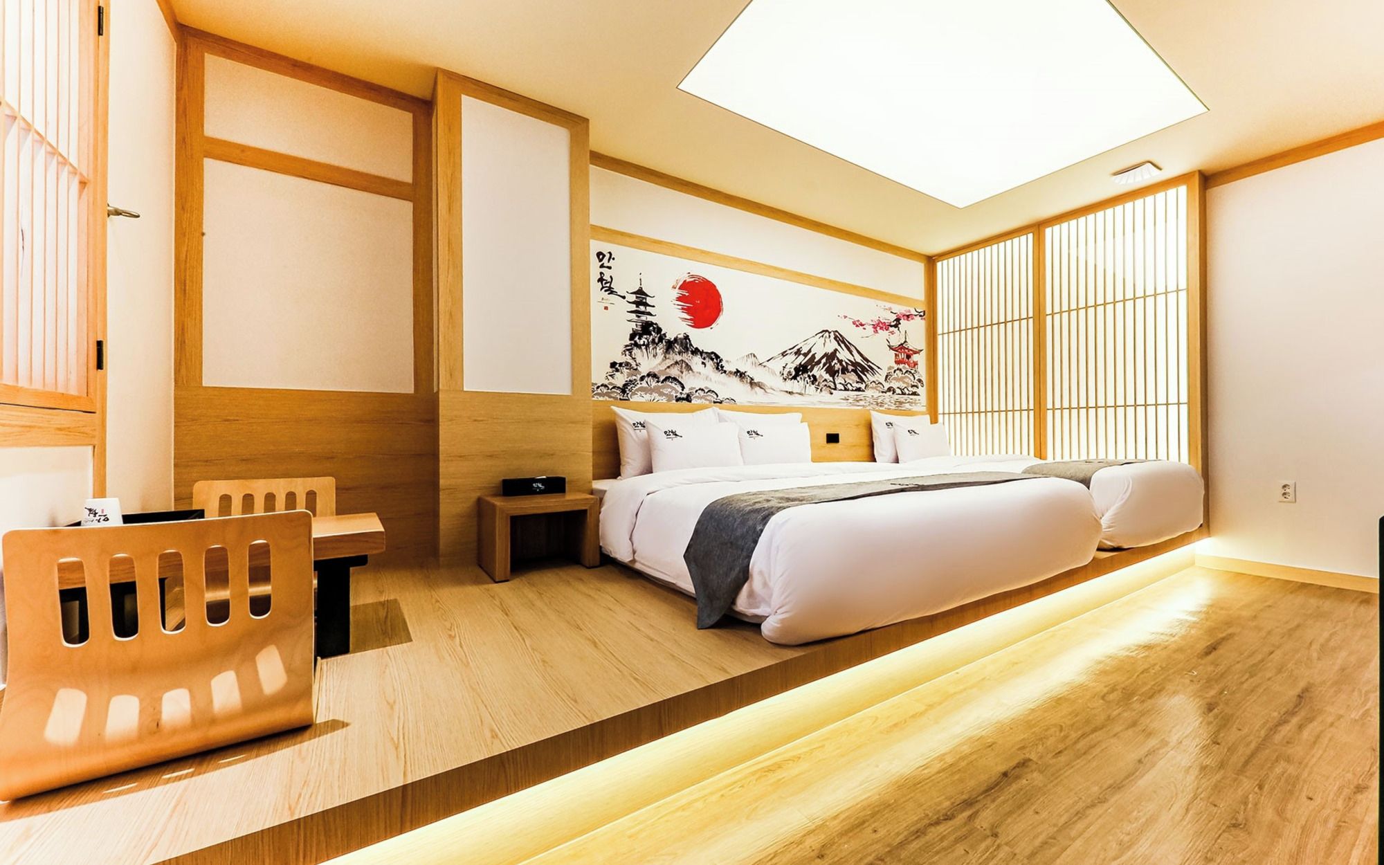 A modern hotel room with a bed, bedside table, and a desk with a chair.