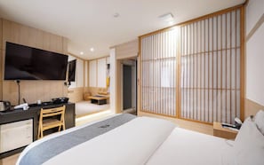 Quarto de hotel com cama, escrivaninha com cadeira, televisão e um painel deslizante estilo shoji.