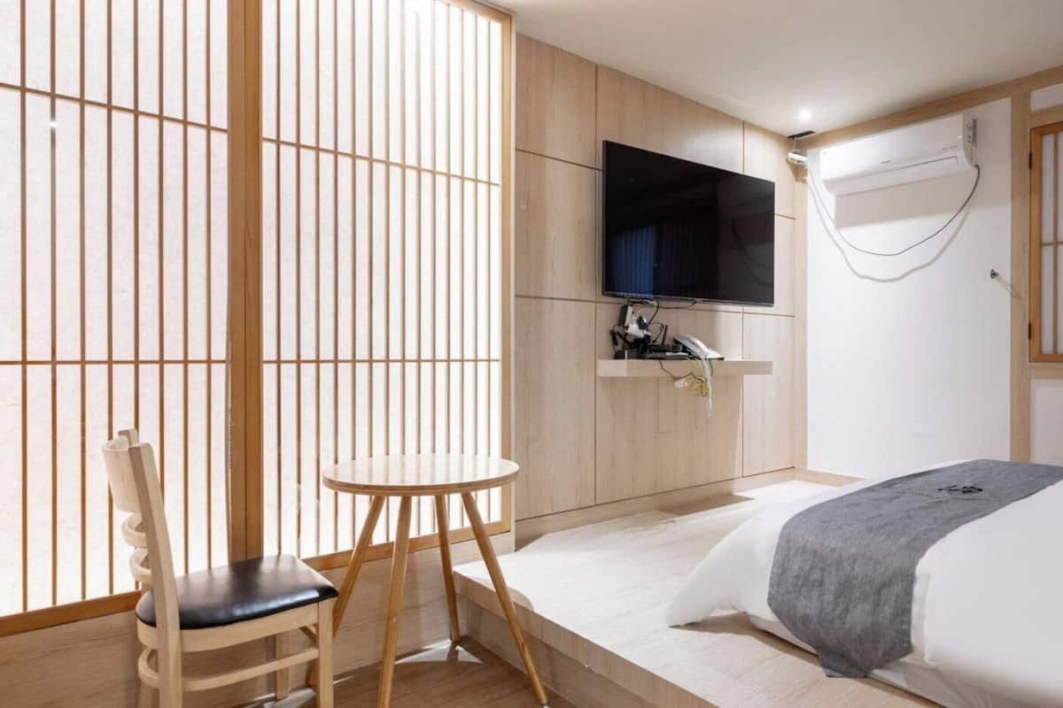 A hotel room with a bed, a TV mounted on the wall, a small table, and a chair.