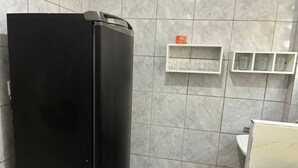 A bathroom with a black refrigerator, tiled walls, a white sink, and shelves with glassware.