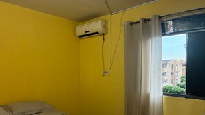 A room with a bed, an air conditioning unit, and a window with curtains.