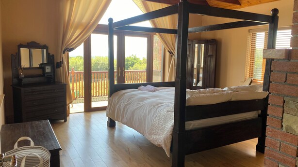 A four-poster bed with a wooden headboard, a dresser with drawers, a mirror, and a wicker basket. - Hilltop house (castlemaine co Kerry)