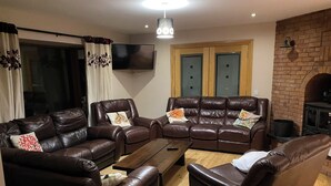 A living room with leather sofas, a flat-screen TV, a wooden coffee table, and a brick fireplace. - Hilltop house (castlemaine co Kerry)