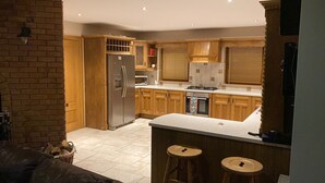 A kitchen with wooden cabinets, a stainless steel refrigerator, a microwave, and a stove. There are two stools at the counter. - Hilltop house (castlemaine co Kerry)