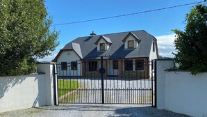 A gated property with a gravel driveway, a white building with a grey roof, and a clear blue sky. - Hilltop house (castlemaine co Kerry)