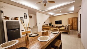 Une cuisine moderne dotée d’un réfrigérateur encastré, d’une table à manger en bois avec des sets de table, et d’un escalier menant à un espace de vie équipé d’un téléviseur.