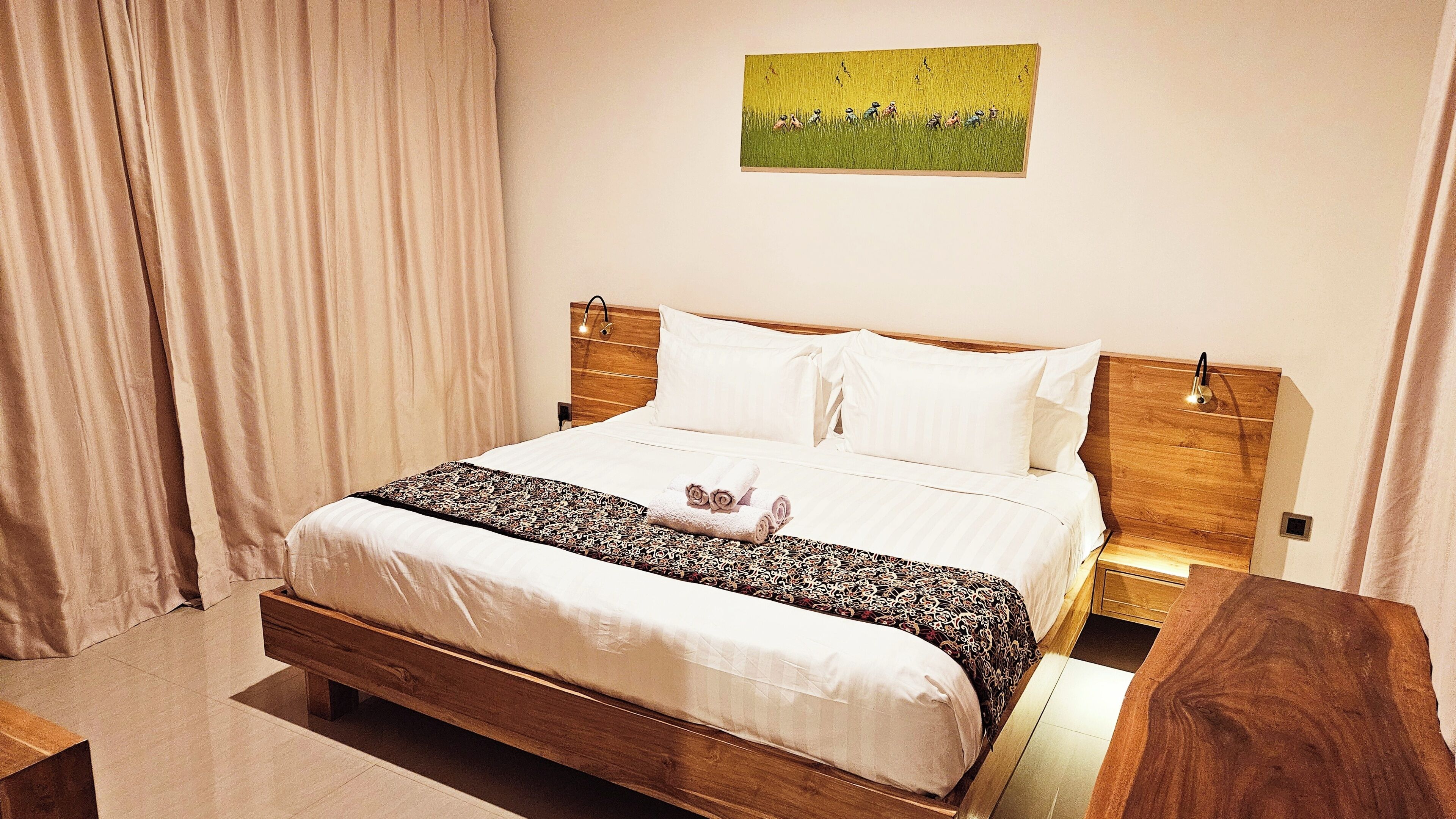 Un letto ben rifatto con lenzuola bianche e una coperta decorata, una testiera in legno, comodini e un quadro raffigurante un campo sulla parete.