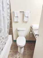 Un baño con inodoro, toallero con dos toallas y cortina de ducha con estampado de hojas.