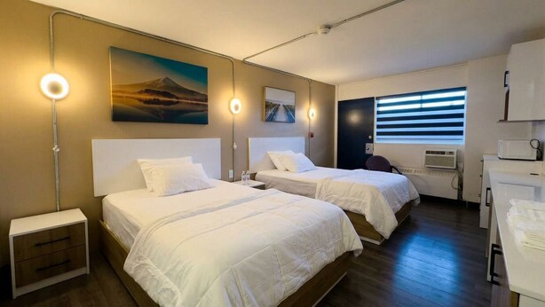 Habitación de hotel con dos camas, un escritorio, una silla, un televisor de pantalla plana y una ventana con persianas.