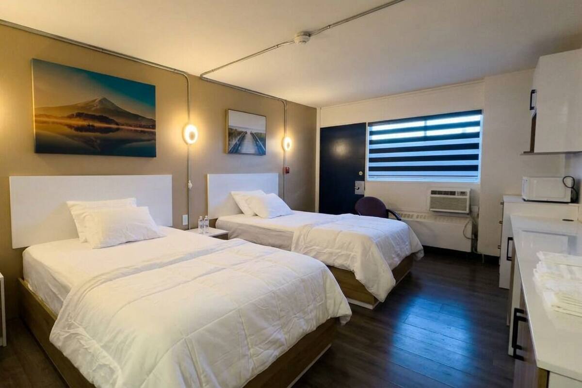 A hotel room with two beds, a desk, a chair, a flat-screen TV, and a window with blinds.