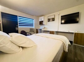 Una habitación de hotel con cama, escritorio, televisor y ventana con persianas.