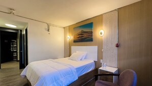 Una habitación de hotel con cama, una silla, un cuadro y una mesita de noche.