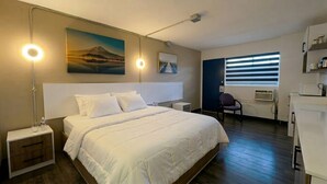 Habitación de hotel con cama, lámparas de noche, una silla, escritorio y ventana con persianas.