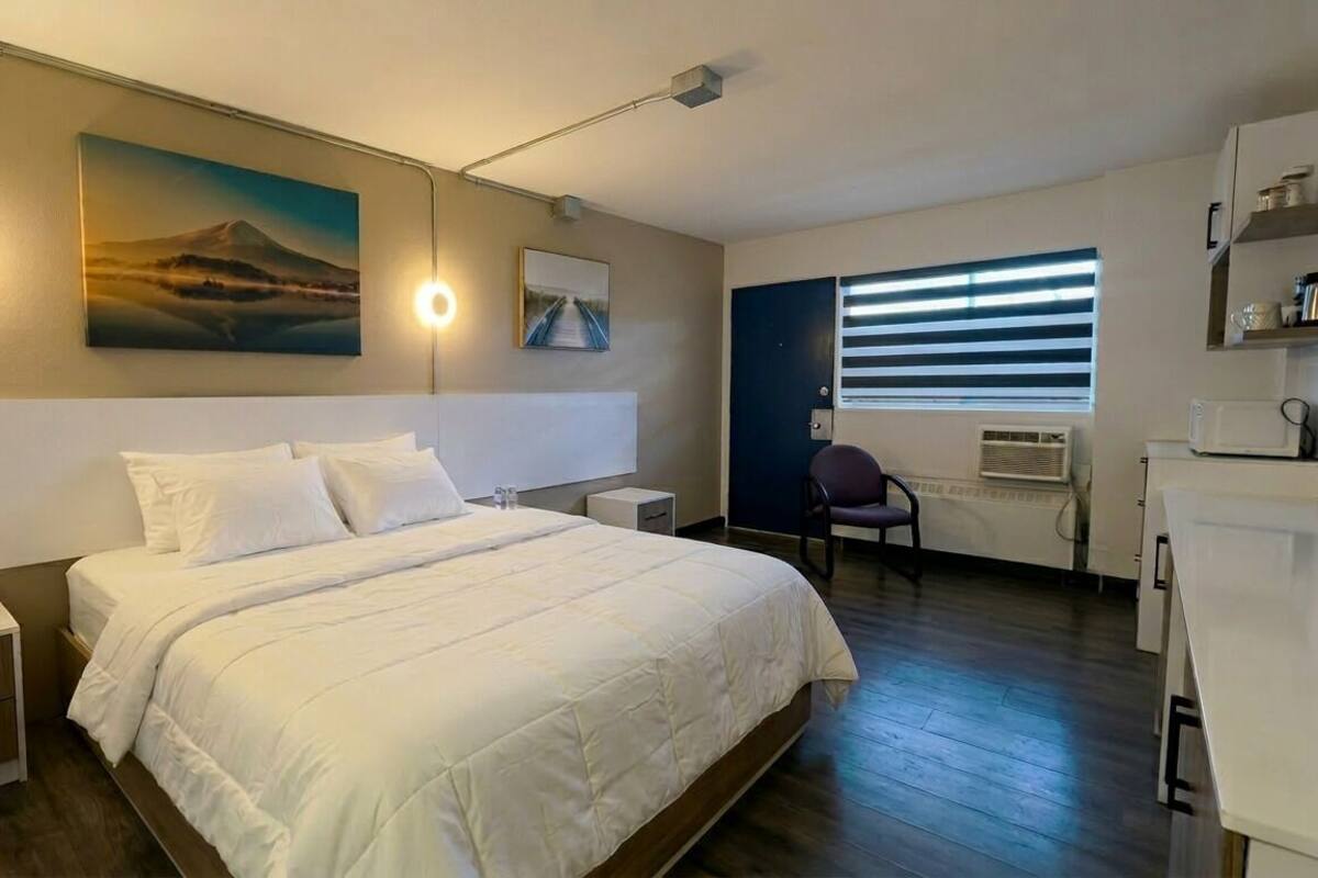 A hotel room with a bed, bedside lamps, a chair, a desk, and a window with blinds.