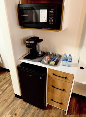 Una kitchenette compacta con microondas, cafetera y un refrigerador pequeño.