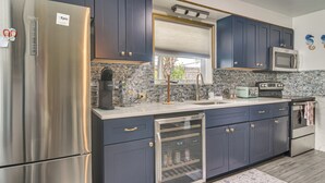A modern kitchen with stainless steel appliances, dark blue cabinets, a built-in microwave, and a window with a view. - Near Beach & Corey Ave! Walkable Snowbird Escape (St Pete Beach)