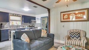 A modern kitchen with dark blue cabinets, a microwave, and a dining area with a gray sofa and striped armchair. - Near Beach & Corey Ave! Walkable Snowbird Escape (St Pete Beach)