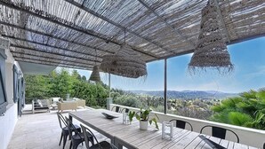 Un patio esterno con tavolo e sedie in legno, un cesto appeso e vista sul paesaggio.