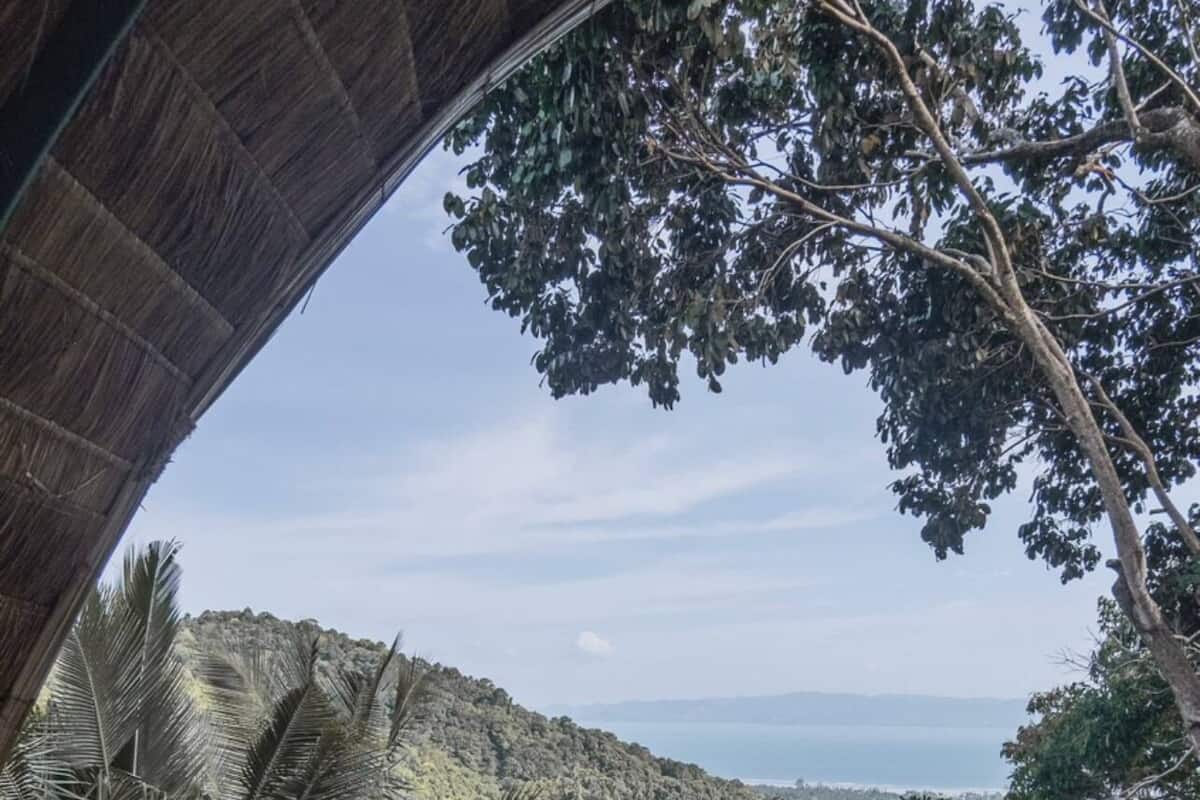 Ein Balkon mit Korbmöbeln, der auf eine gebirgige Landschaft und ein Gewässer blickt.