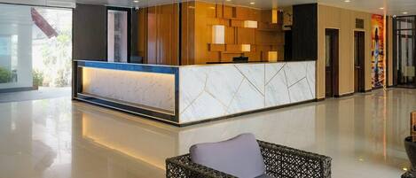 A modern hotel lobby with a reception desk, a chandelier, and a seating area.