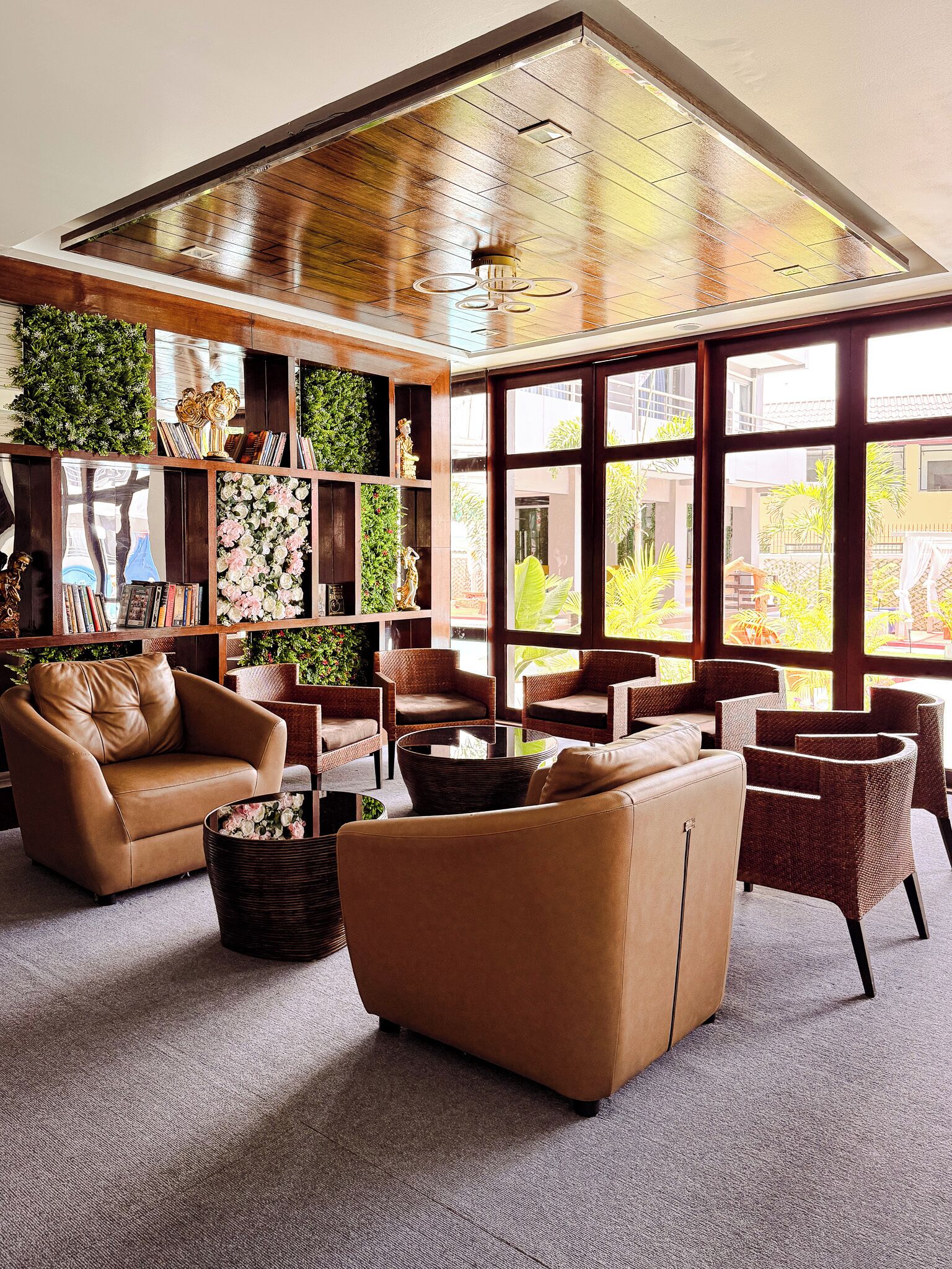 A spacious lounge area with leather sofas, wicker chairs, and a large window offering a view of the outdoors.