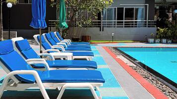 A poolside area with lounge chairs and umbrellas, a swimming pool, and a building with multiple windows and balconies.