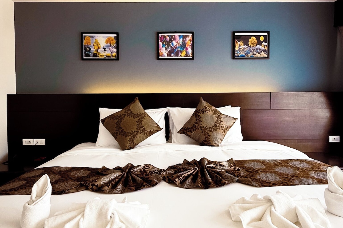 A neatly made bed with pillows, a blanket, and towels arranged on a hotel room.