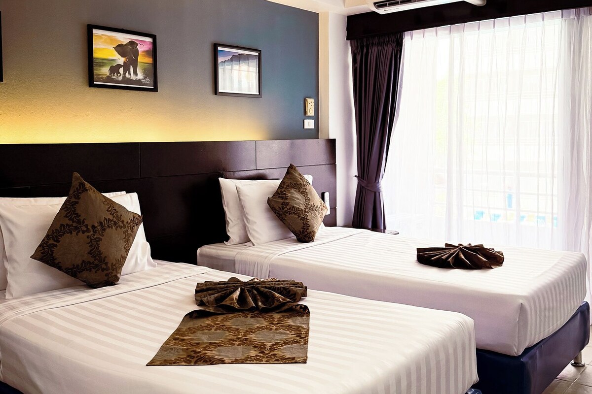 A hotel room with two beds, a headboard, a wall-mounted air conditioner, and a window with curtains.