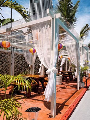 Un espacio de estar al aire libre techado con mesas y sillas, techo de cristal y faroles decorativos.