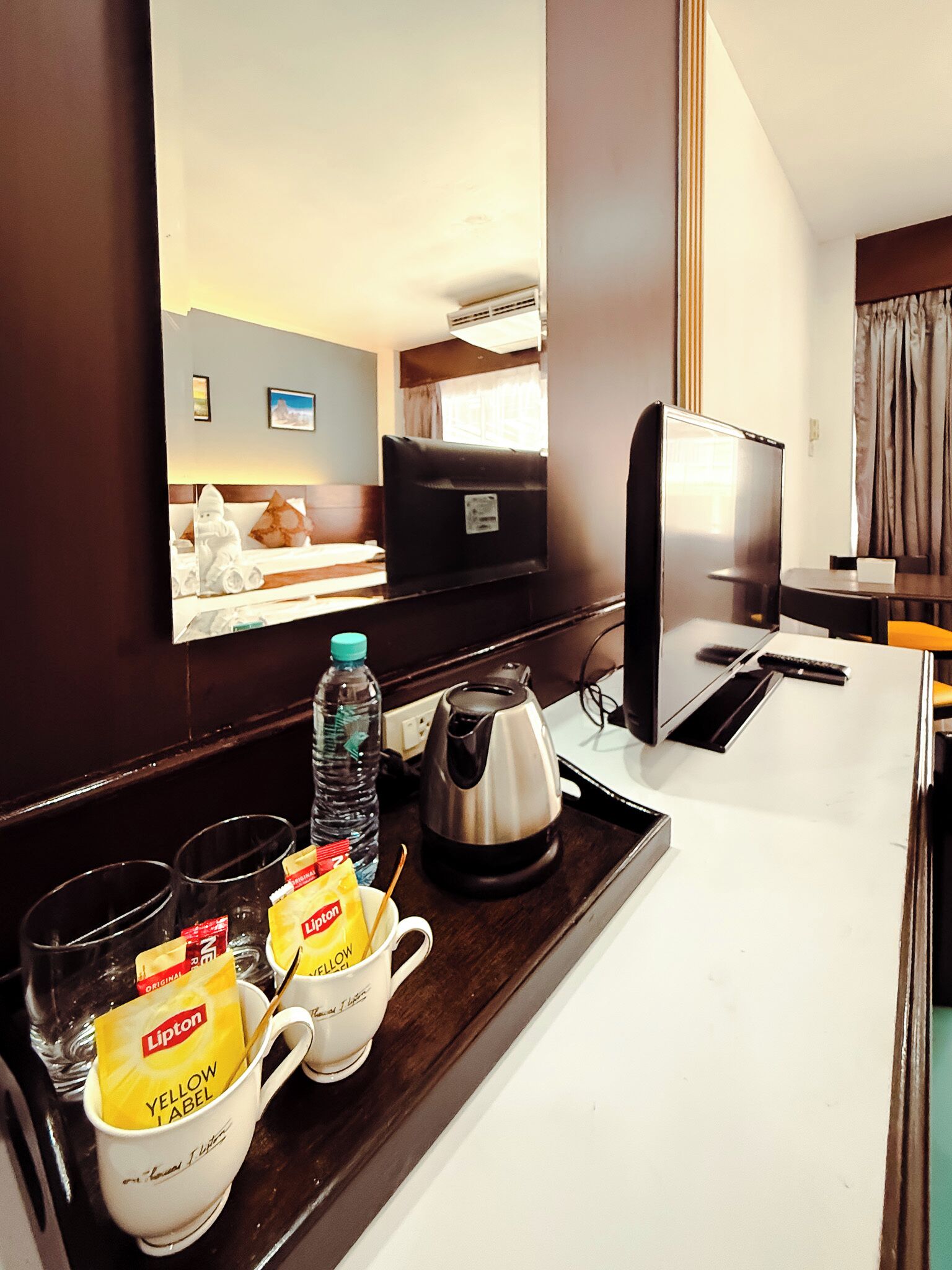 A hotel room with a desk, a kettle, a bottle of water, and Lipton tea bags.