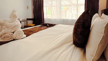 A hotel room with a bed, a window with curtains, an air conditioning unit, and a chair.